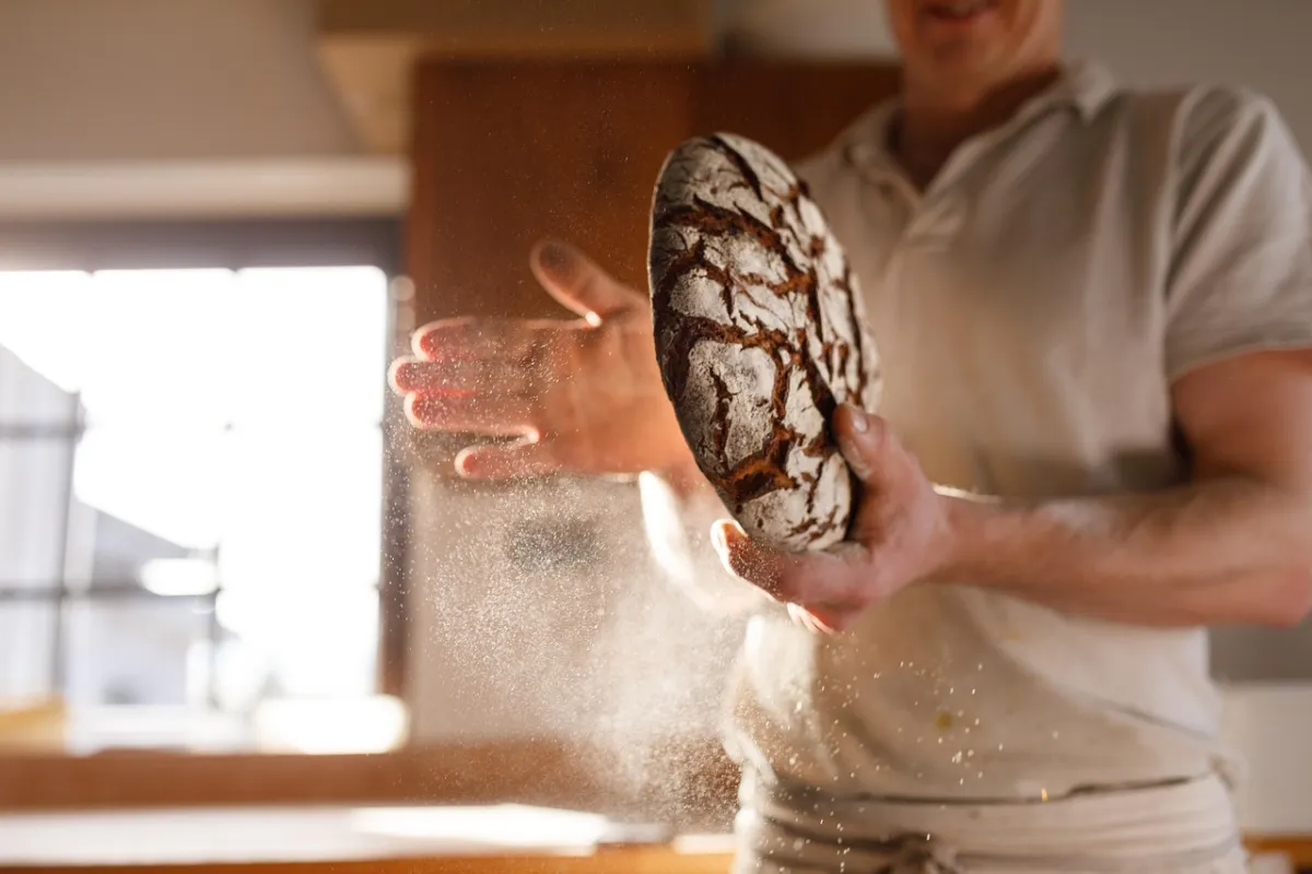 Boulanger saupoudrant de farine un pain artisanal